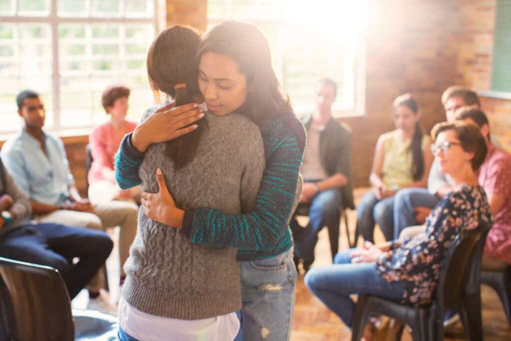 A person experiencing crystal meth psychosis receives comfort through a supportive embrace during a group therapy session.