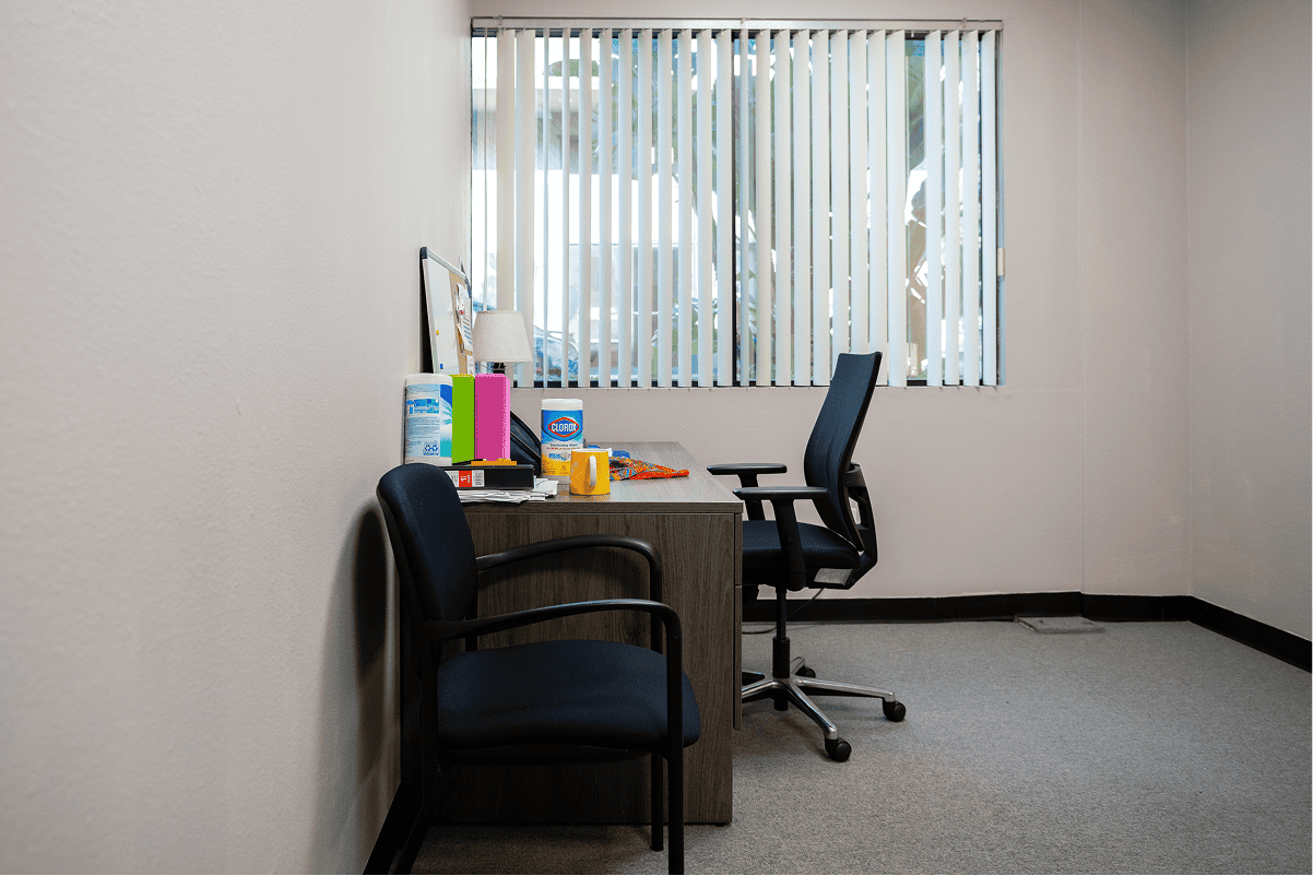 Empty office with desk, chairs, and window blinds for therapy sessions.