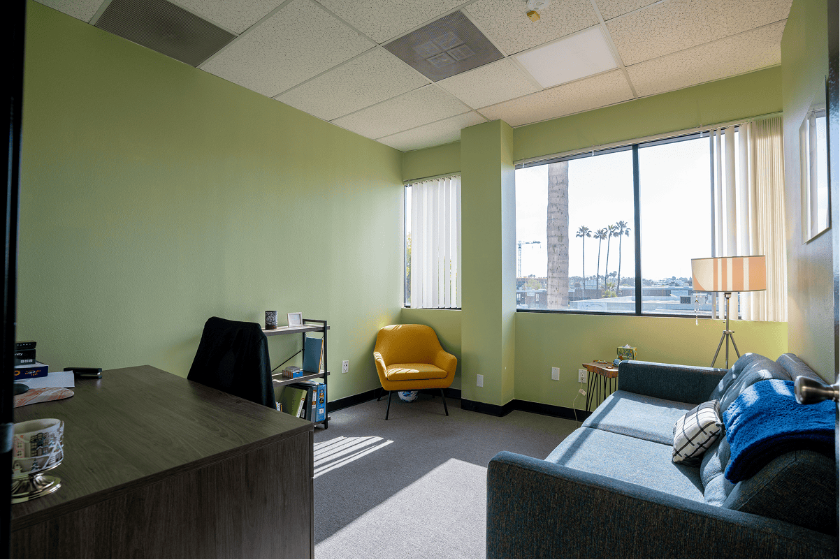 Bright therapy office with green walls, large windows, and comfortable seating.