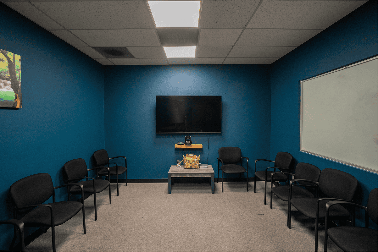 Empty therapy room with chairs, TV, and whiteboard for addiction treatment.